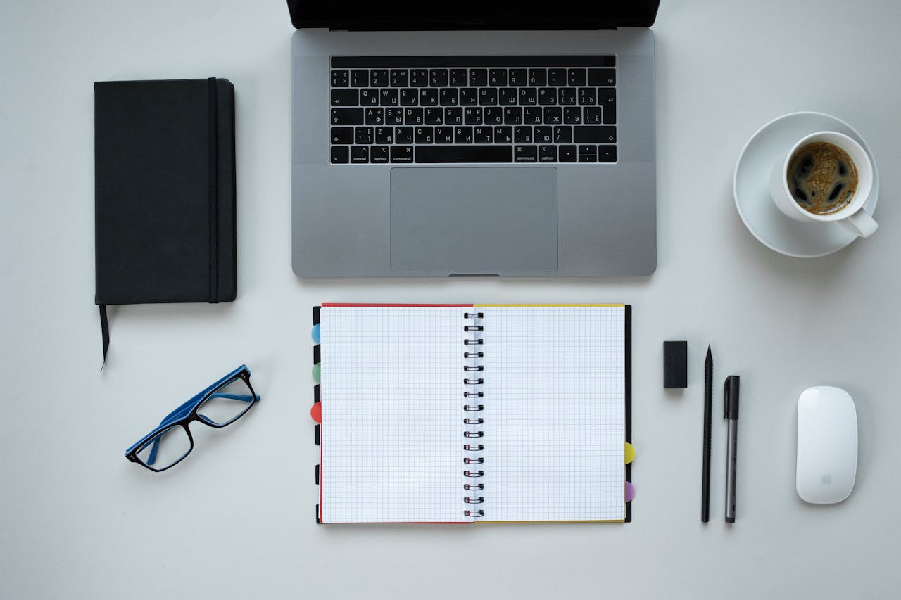 Top view of a desk with laptop, notebook, coffee, and office supplies, perfect for remote work theme.